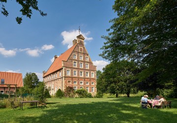 Das Haus Brückhausen mit weitläufigem Garten, in dem vier Menschen gemeinsam an einem Gartentisch sitzen.