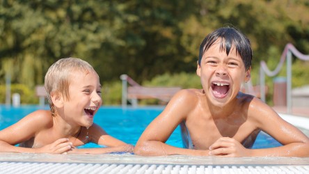 Zwei lachende Jungs lehnen am Beckenrand eines Freibadbeckens.